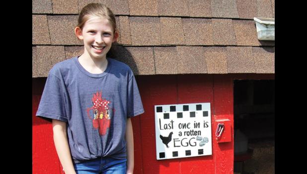 Kelly stands net to the "Last one in is a rotten egg" sign beside the door of the coop where the chickens roost each night. Mascot photo by Scott Thoma