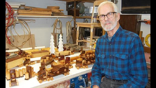 Staff photo by Scott Thoma. Myrvik sits by some of the many wooden toy vehicles he has made, including a forklift on the left and his logging trucks in the back.