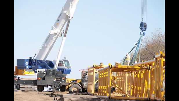 Staff Photo by Byron Higgin. A trucker hauls the turbine stack into the field and below that a worker attaches the crane to some of the scaffolding